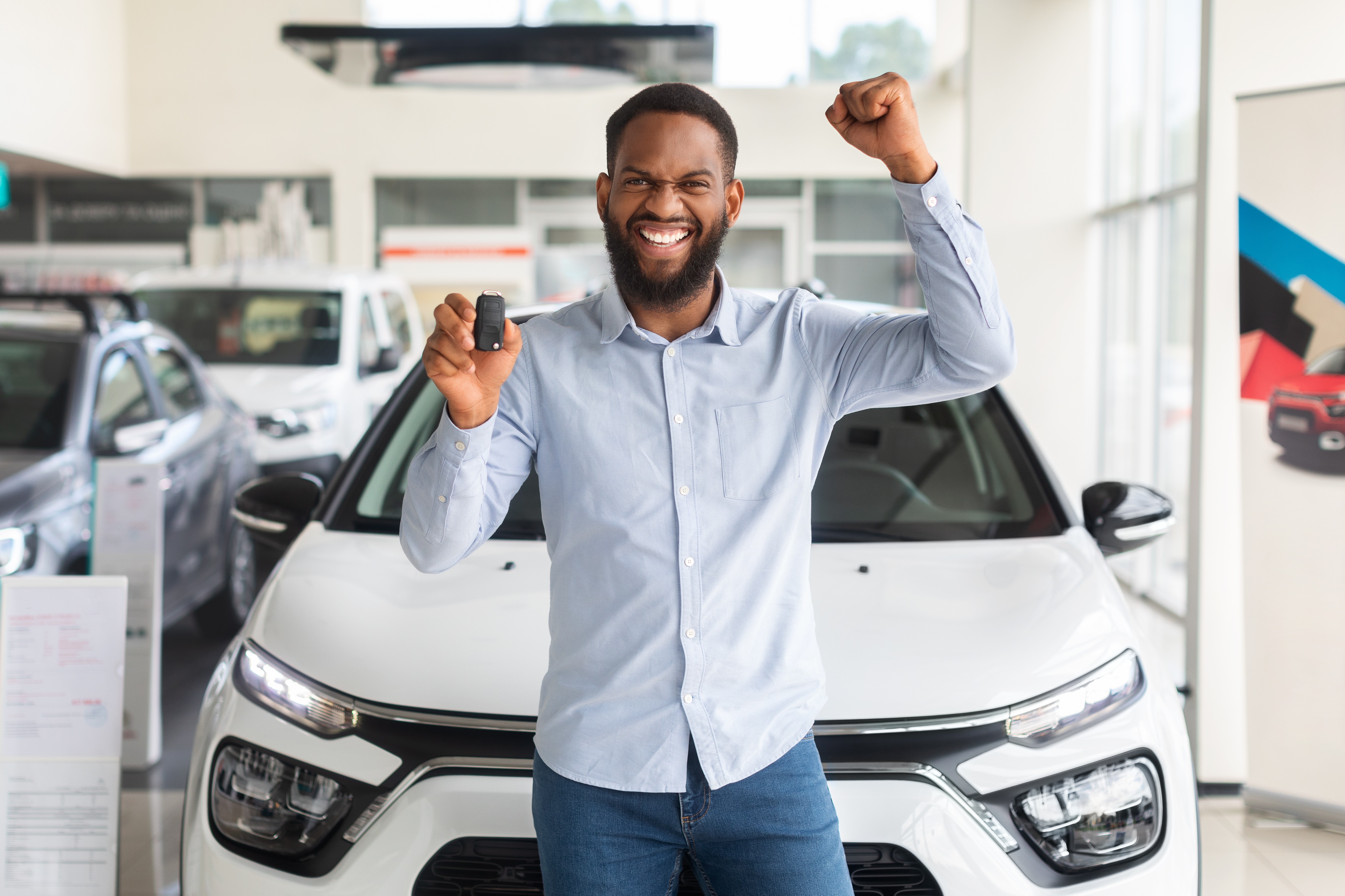 Homem comemora a compra do carro novo segurando a chave em concessionária, representando conquista, planejamento financeiro e realização pessoal.