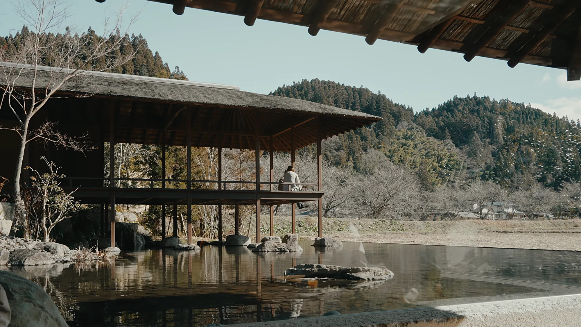 A thatched pavilion over the pond at Kurokawa Onsen, bare winter trees behind