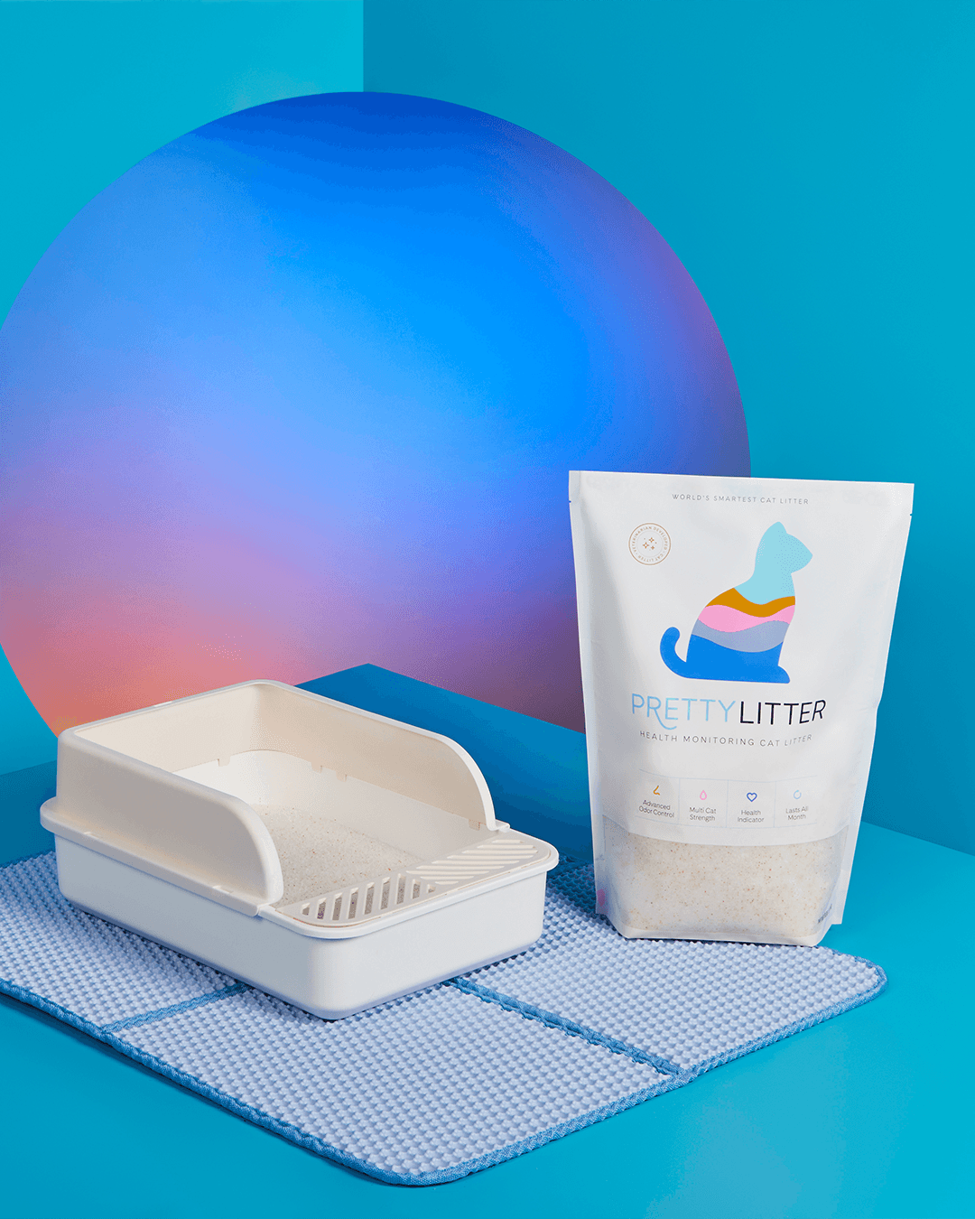 PrettyLitter product packaging, litter box, and litter mat in front of colorful, gradient backdrop