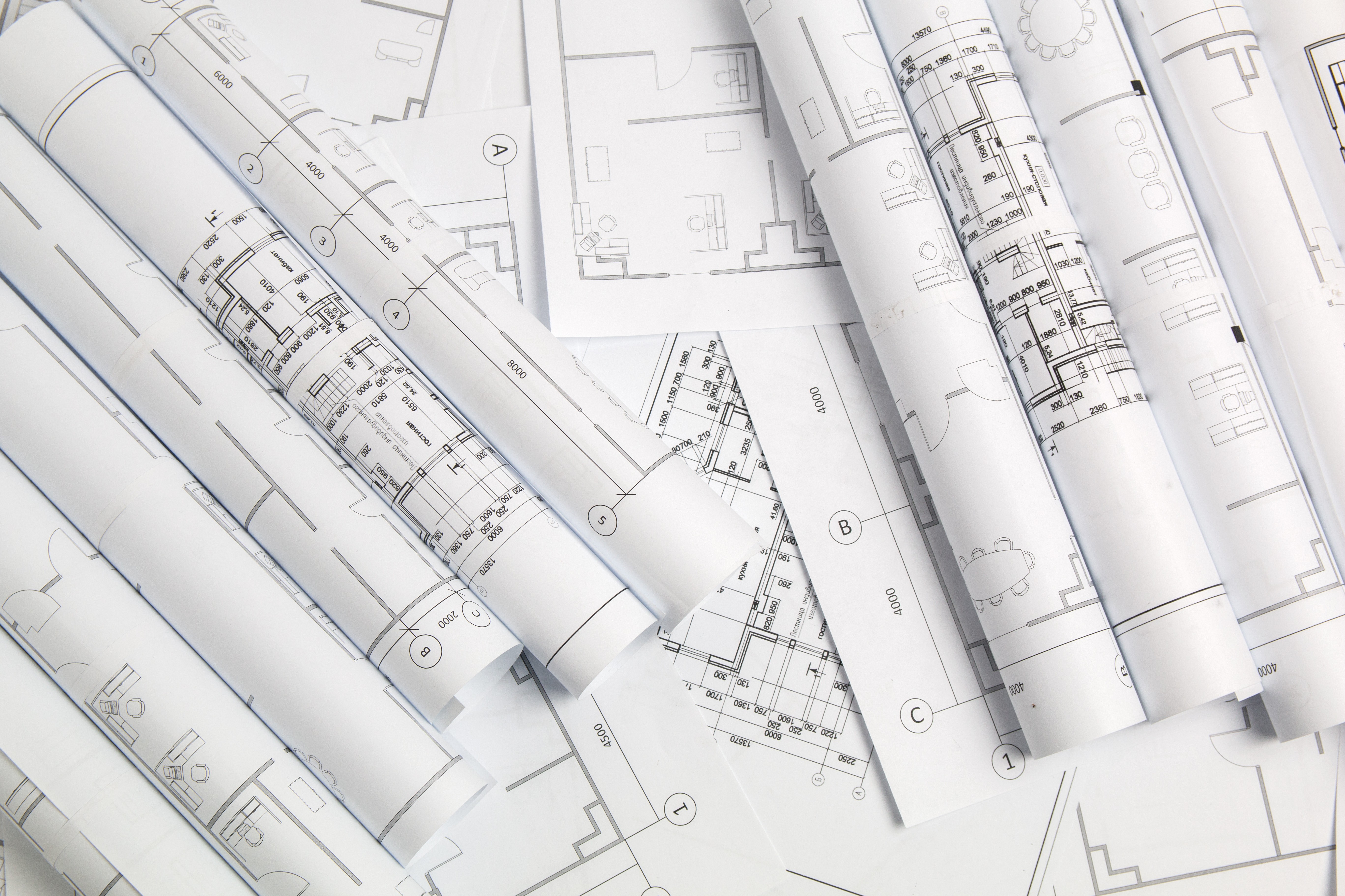 Rolled architectural blueprints with detailed floor plan drawings spread in overlapping layers.