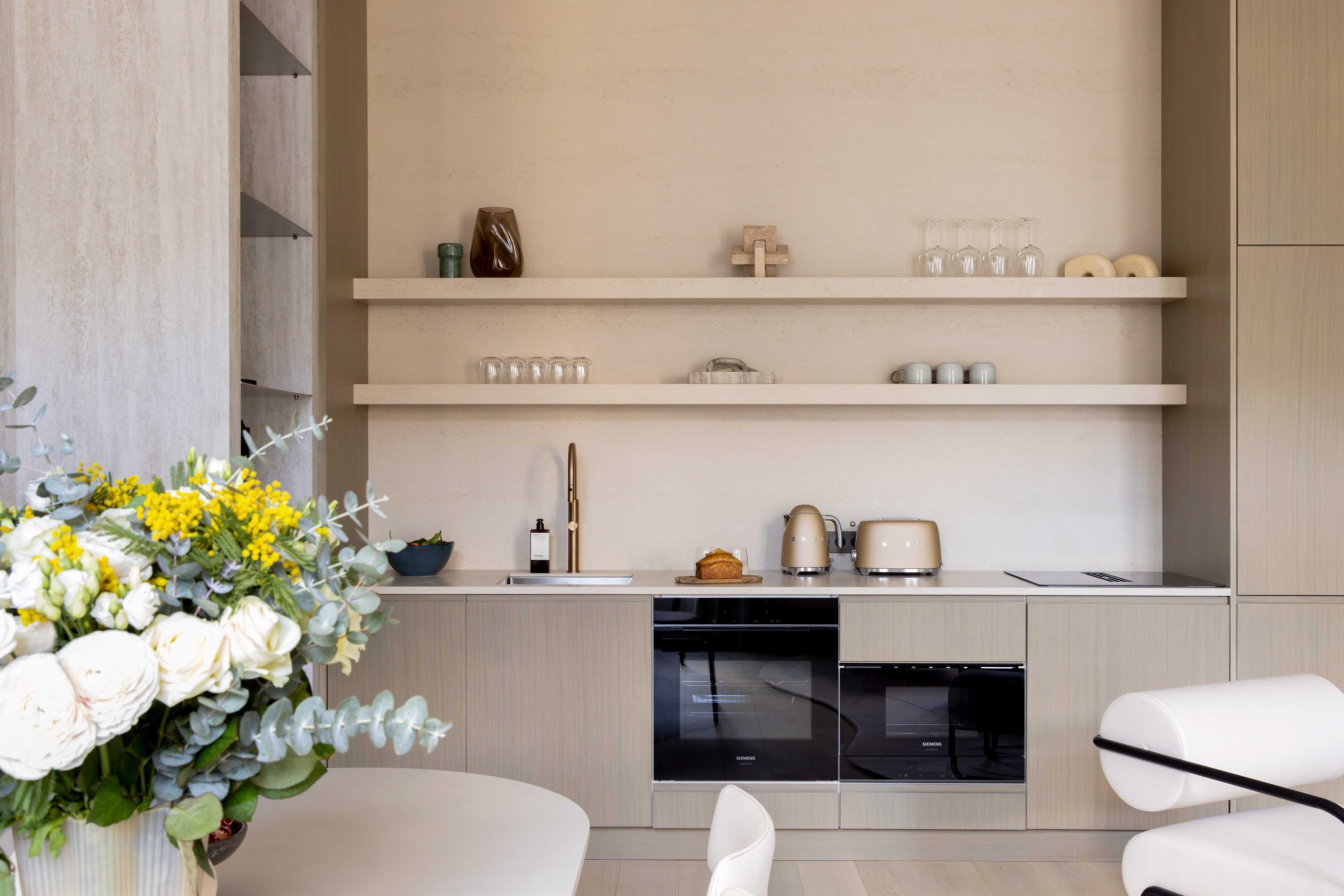 Cuisine ouverte en bois clair avec etageres, robinetterie doree, four noir et bouquet de fleurs jaunes