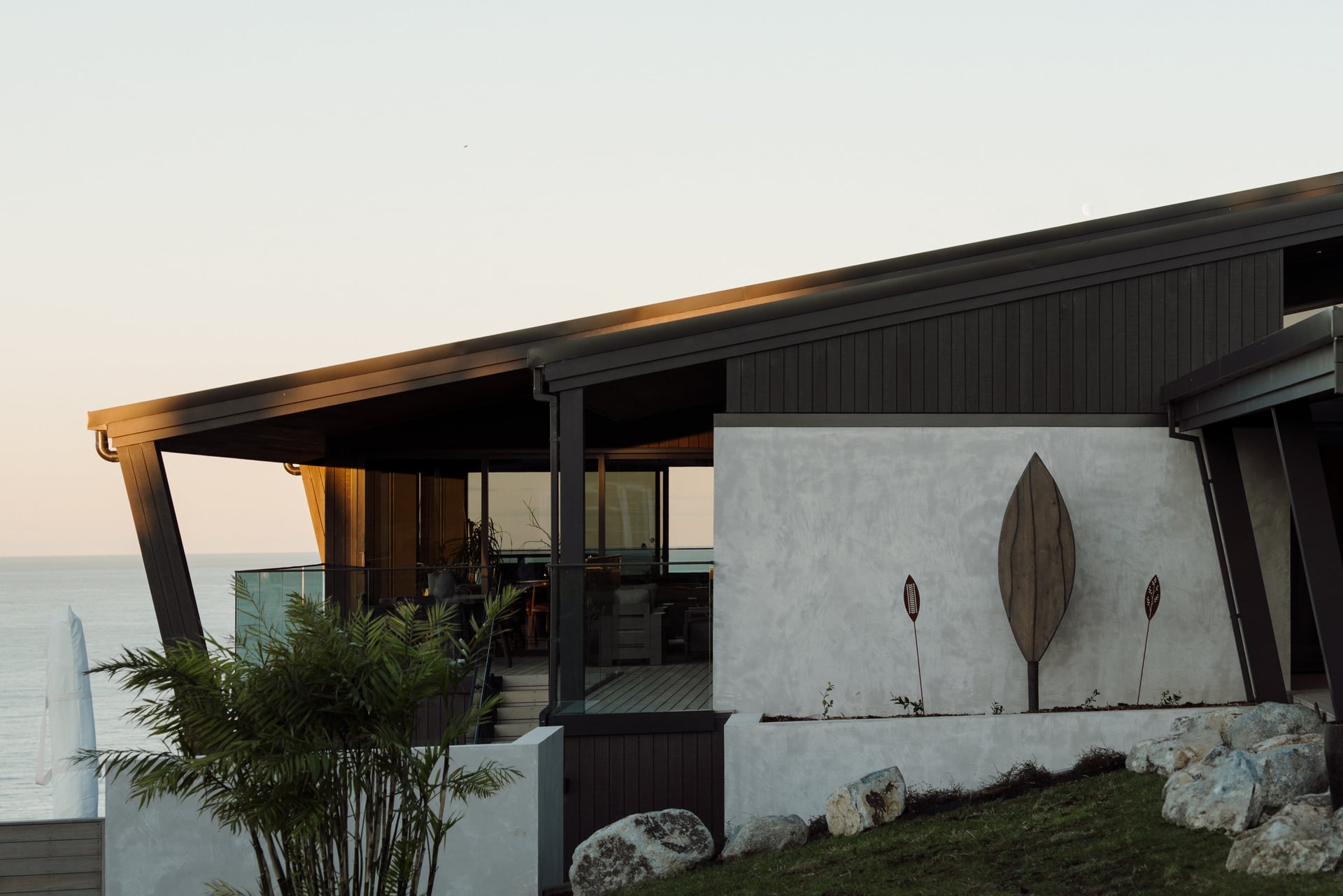 Dark timber home above the sea at dusk, Bay of Plenty