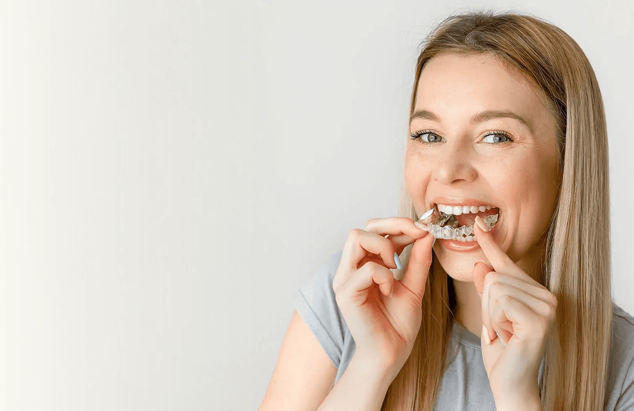 A woman smiles and holds invisalign clear aligners with a case, showcasing a certified invisalign provider at Bella Medical Centre
