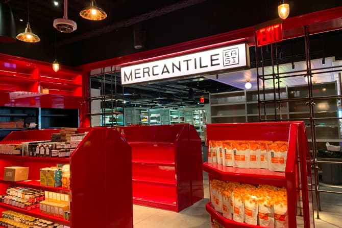 A swanky shop with a large Mercantile sign and small red stands with bodega style goods
