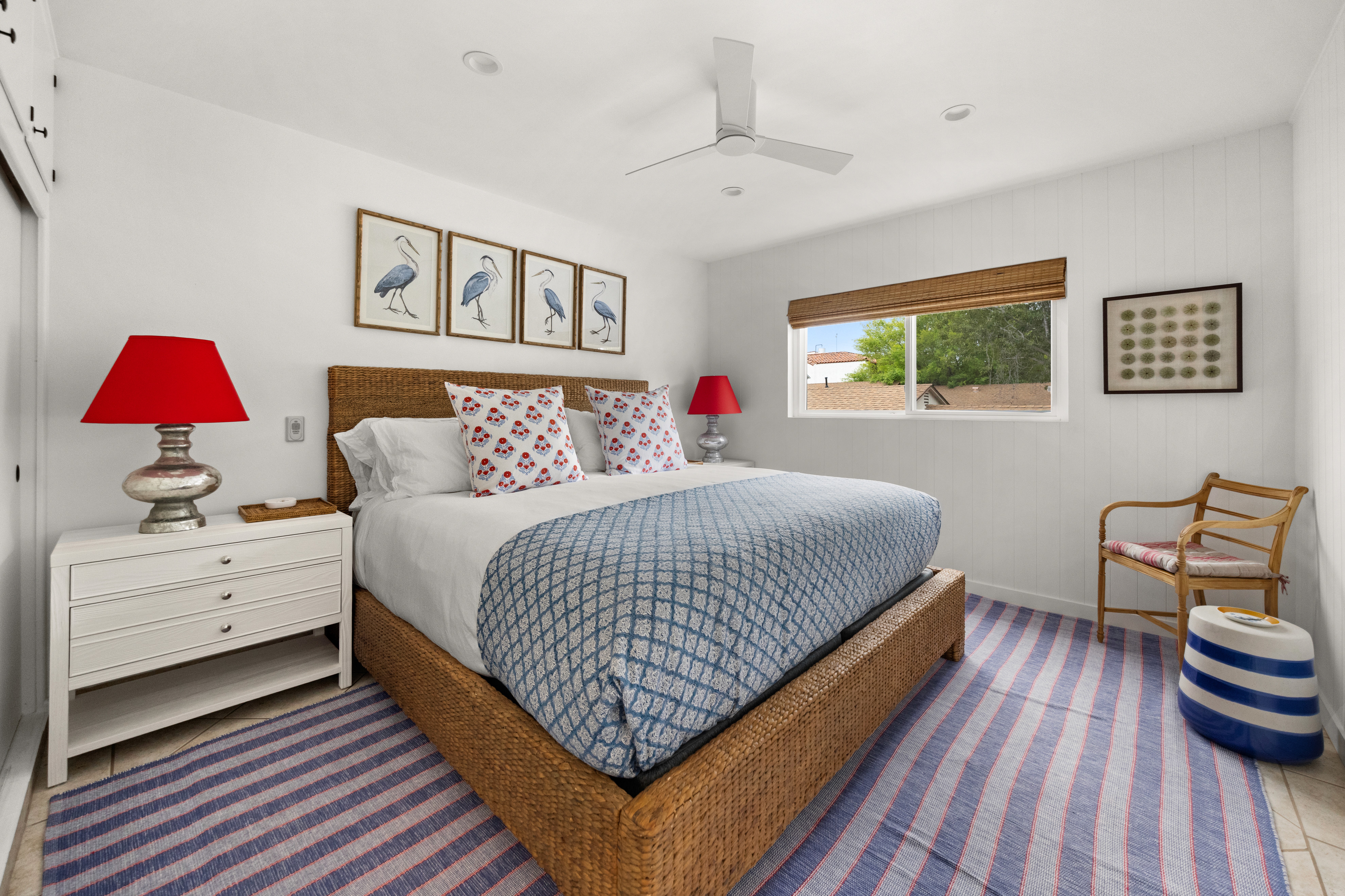 Sunny primary bedroom with a woven bed frame, coastal textiles, and bold red accents for a warm, welcoming feel.