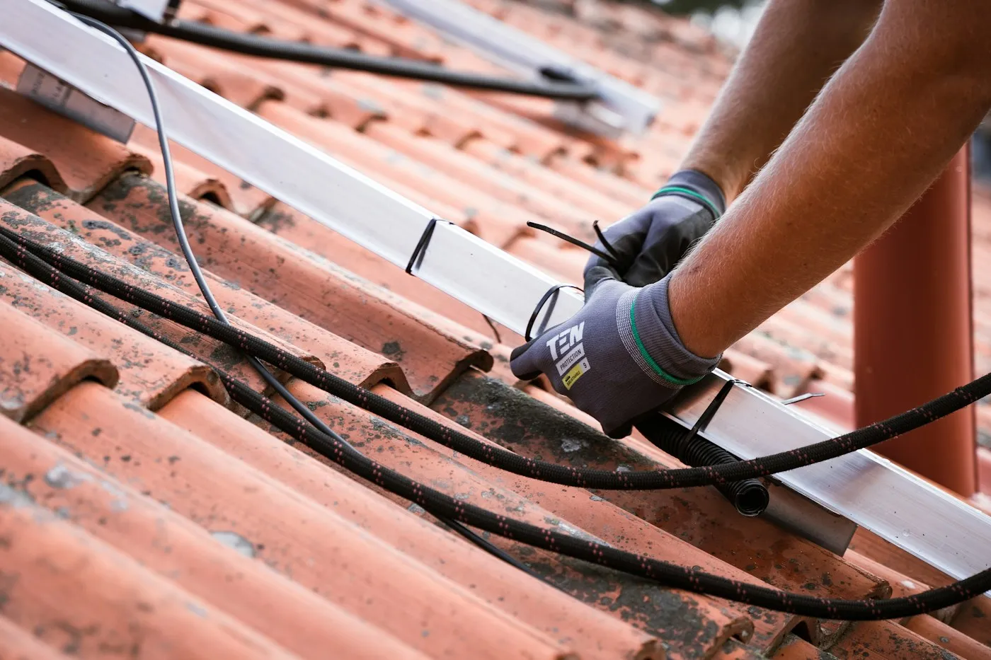 Hand mit Arbeitshandschuhen bei der Kontrolle von Kabeln und Verbindungen an einer Solaranlage