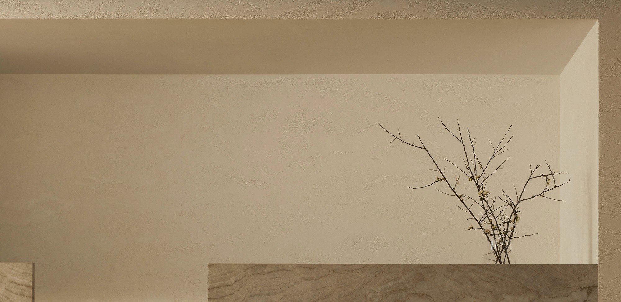 Corner of a room with plastered walls and a bare branch in a vase on a stone ledge