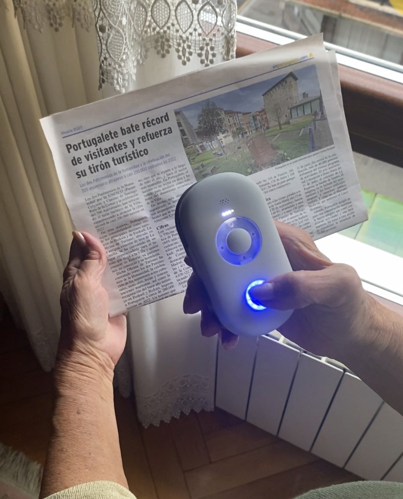 Persona leyendo el periódico con la Lupa Inteligente, que se ilumina mientras lee el texto