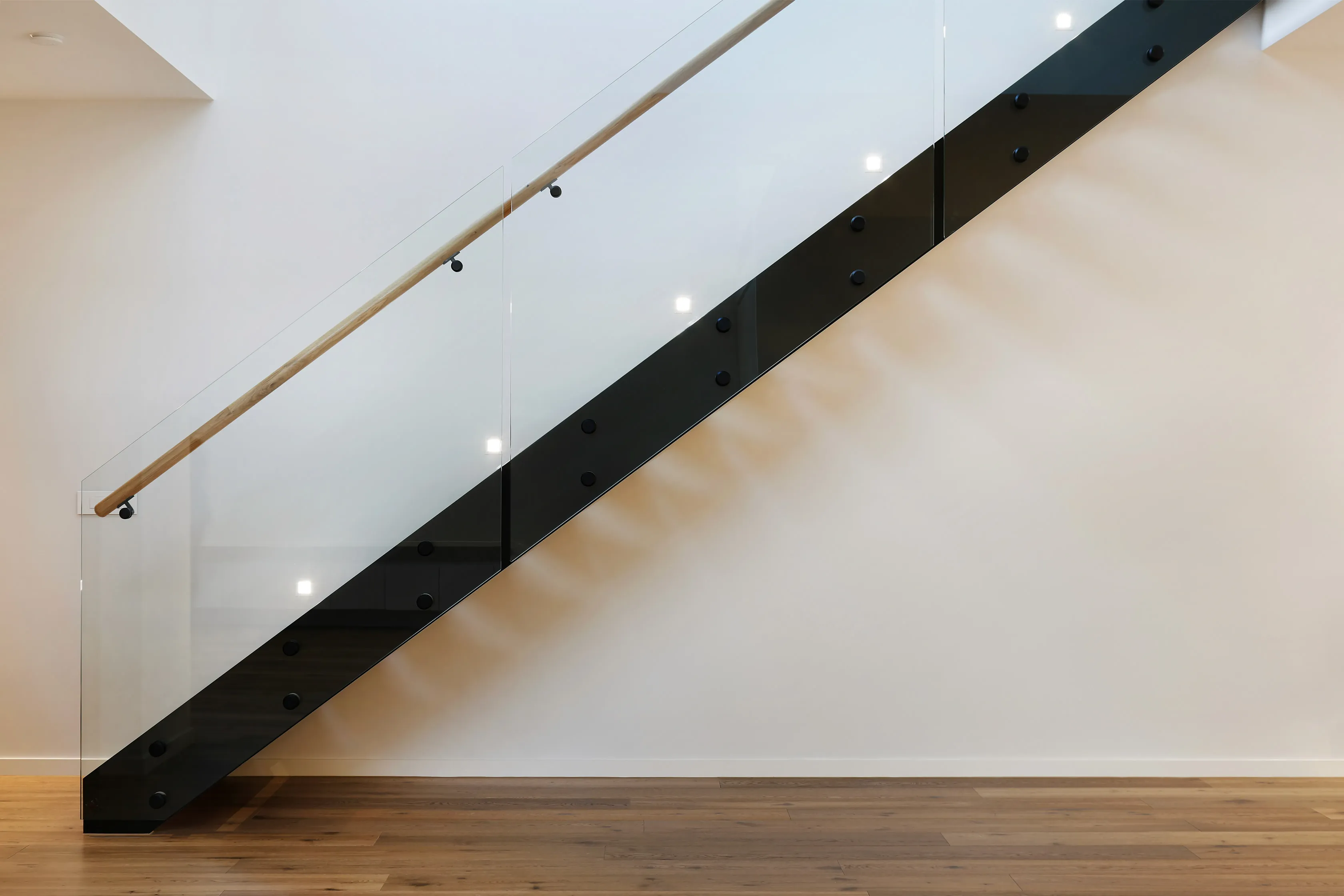 Floating staircase with a smoked-glass and black steel balustrade and oak handrail against a white wall over timber floors