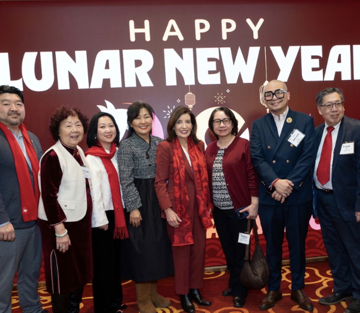 Governor Kathy Hochul, COO Willing Chin-Ma, and others pose in front of a Happy Lunar New Year sign.