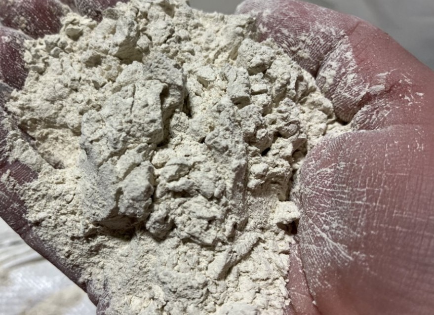Gros plan d'une main tenant une poudre beige granuleuse issue du broyage de céramique recyclée, matière première pour la fabrication de nouveaux matériaux