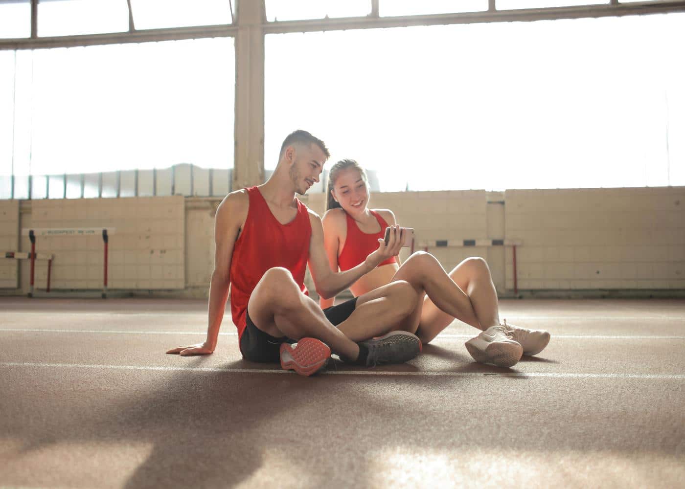 A smiling couple sitting on running track looking at phone