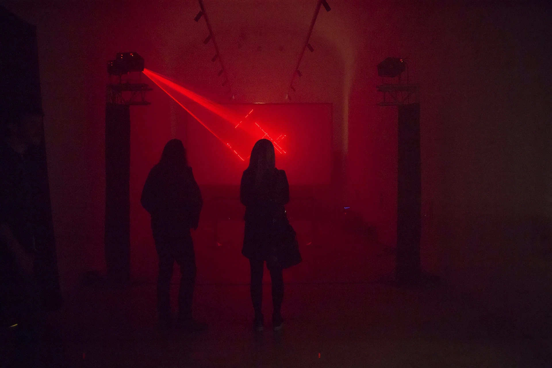 Two people silhouetted against red laser art installation