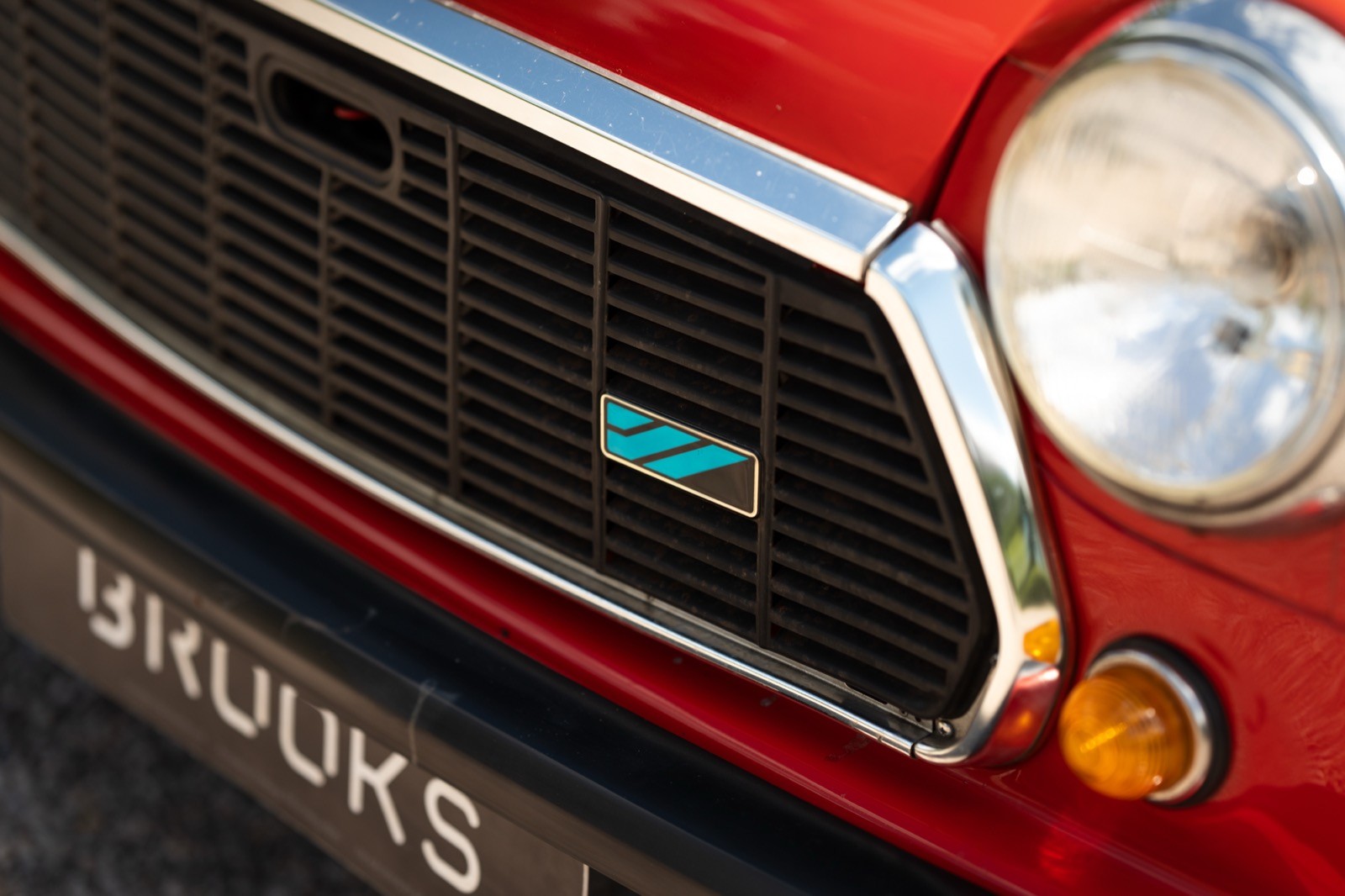Close-up of a red car's front grille and headlight, showcasing the sleek design and shiny details.