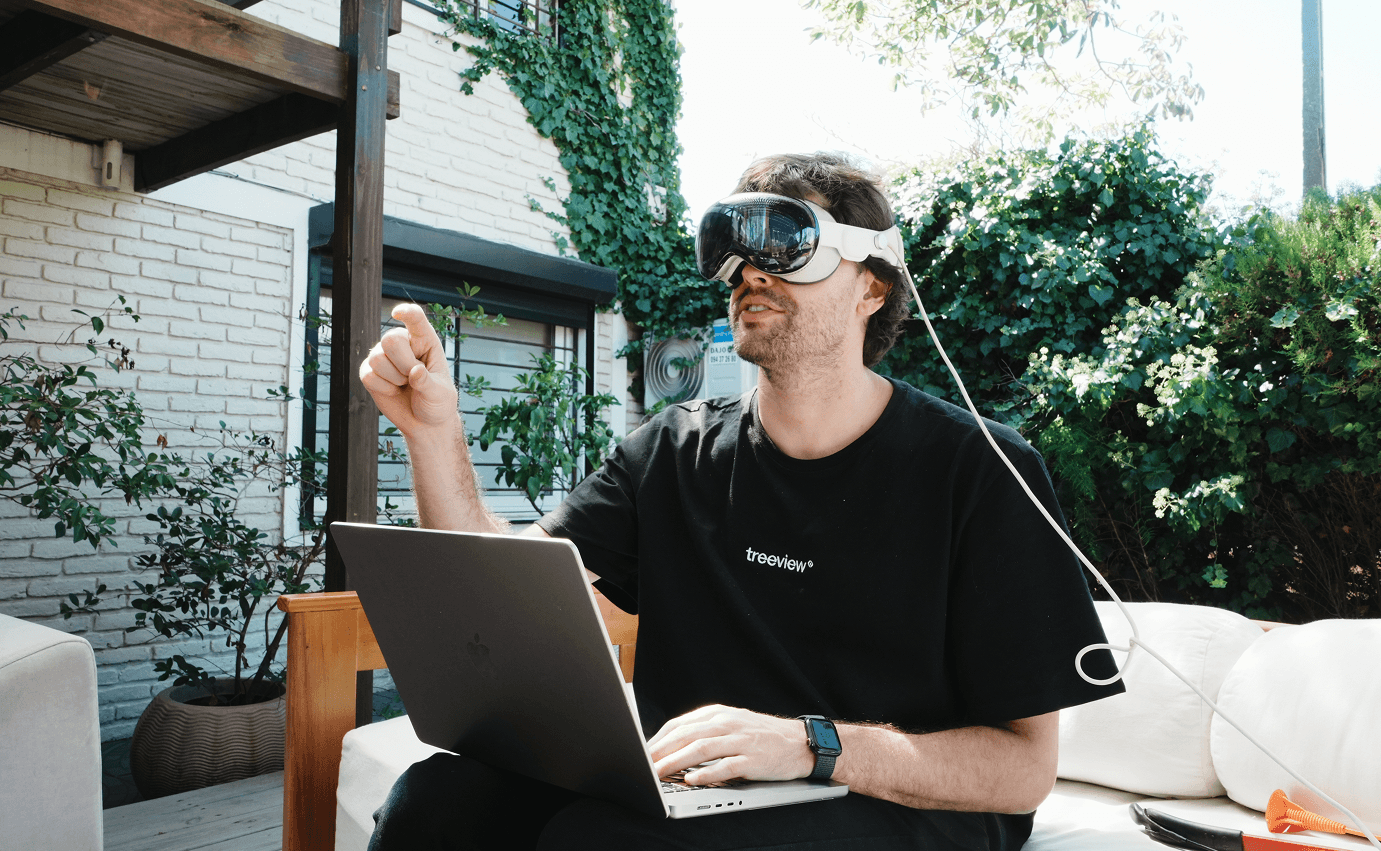 Treeview founder wearing Apple Vision Pro headset while working on a MacBook laptop outdoors, gesturing with one hand in a sunlit garden setting
