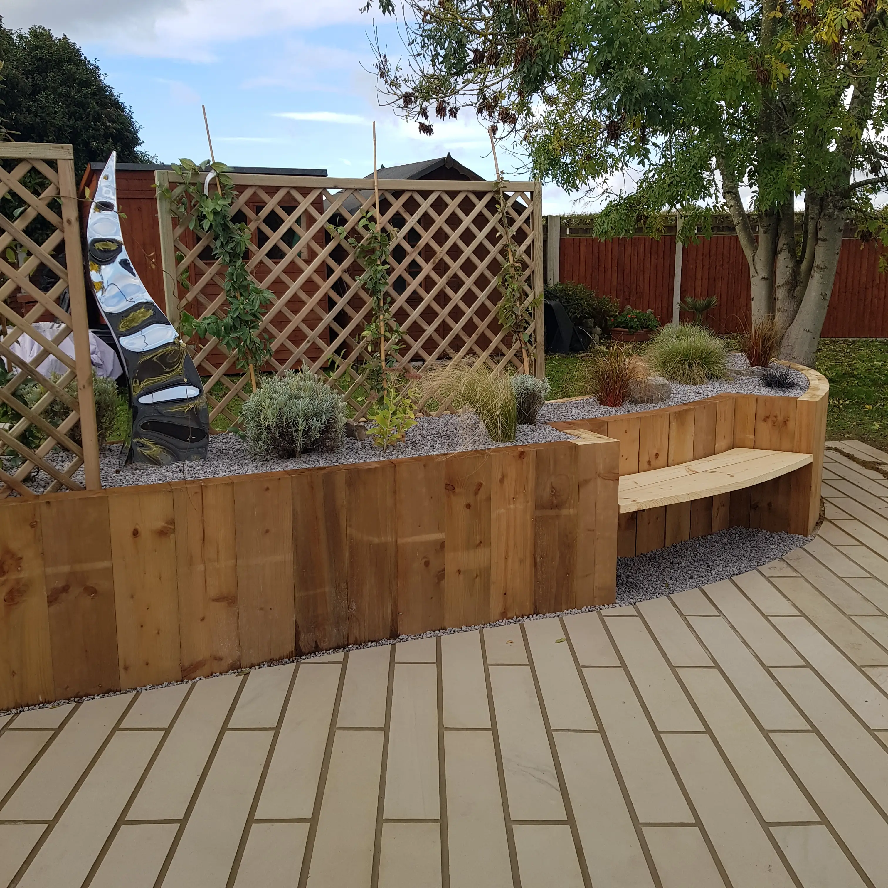 A landscaped garden area featuring wooden planters, a bench, and decorative plants, with a brick pathway.
