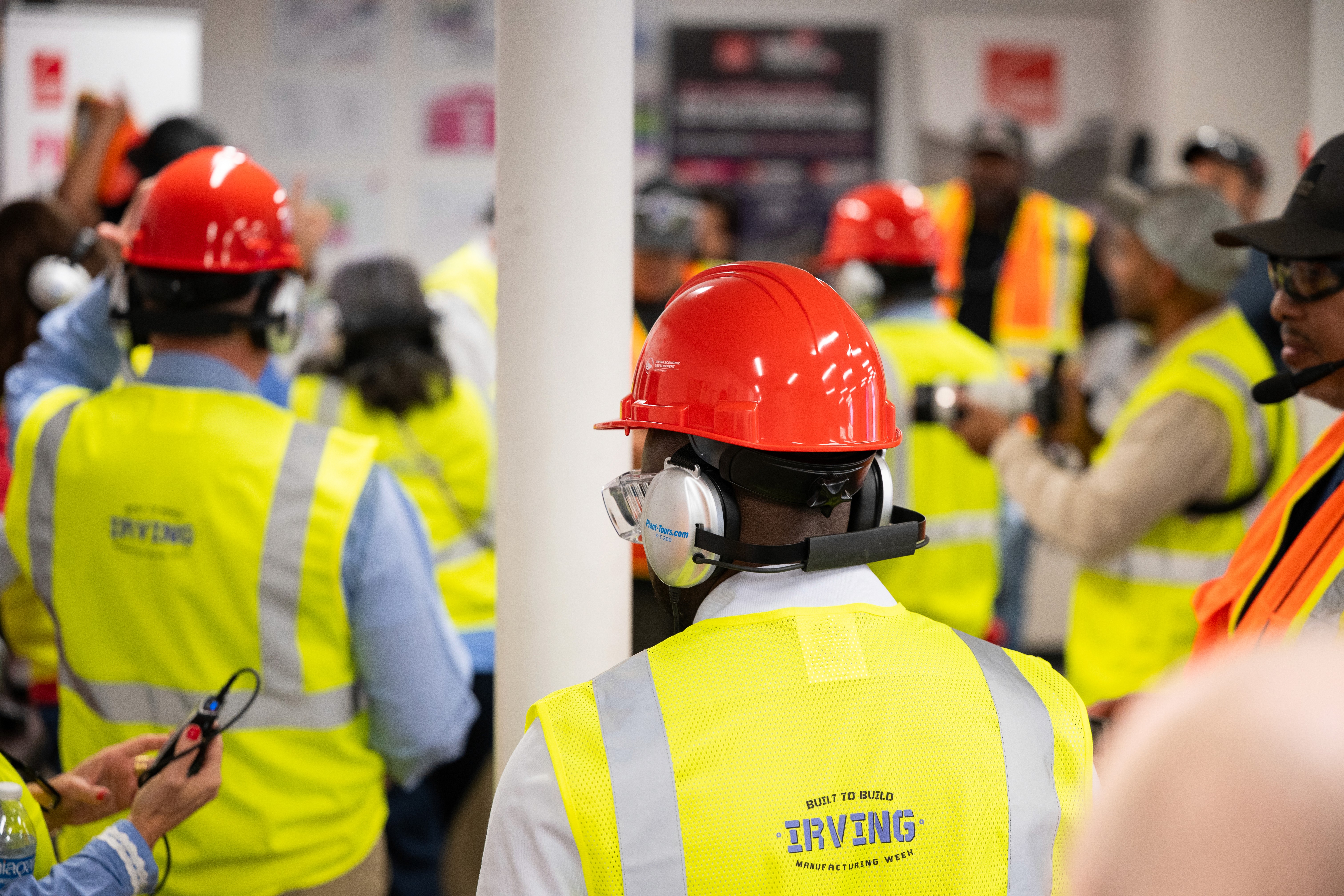 Event photography of a tour group waits to see the manufacturing facility and their processes, while dressed in neon vests and red branded hard hats. 