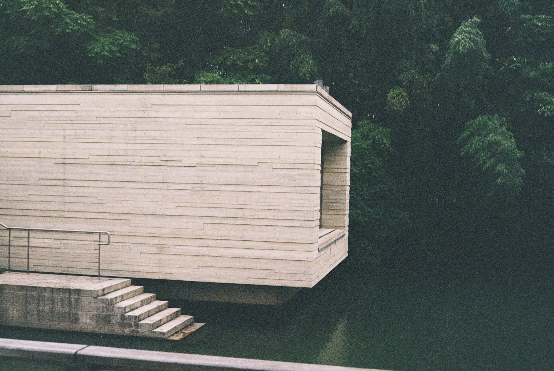 Board-marked concrete pavilion cantilevered over a still river