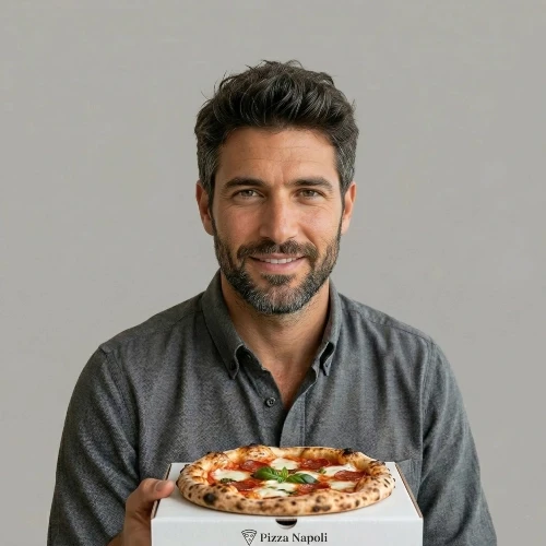 דיוקן של בעלי "פיצה נאפולי", גבר ישראלי צעיר בשנות ה-30 לחייו עם חיוך מזמין, אוחז במגש פיצה טרייה על רקע אפור נקי. תמונת לקוח ממליץ עבור סוכנות DigiGo.