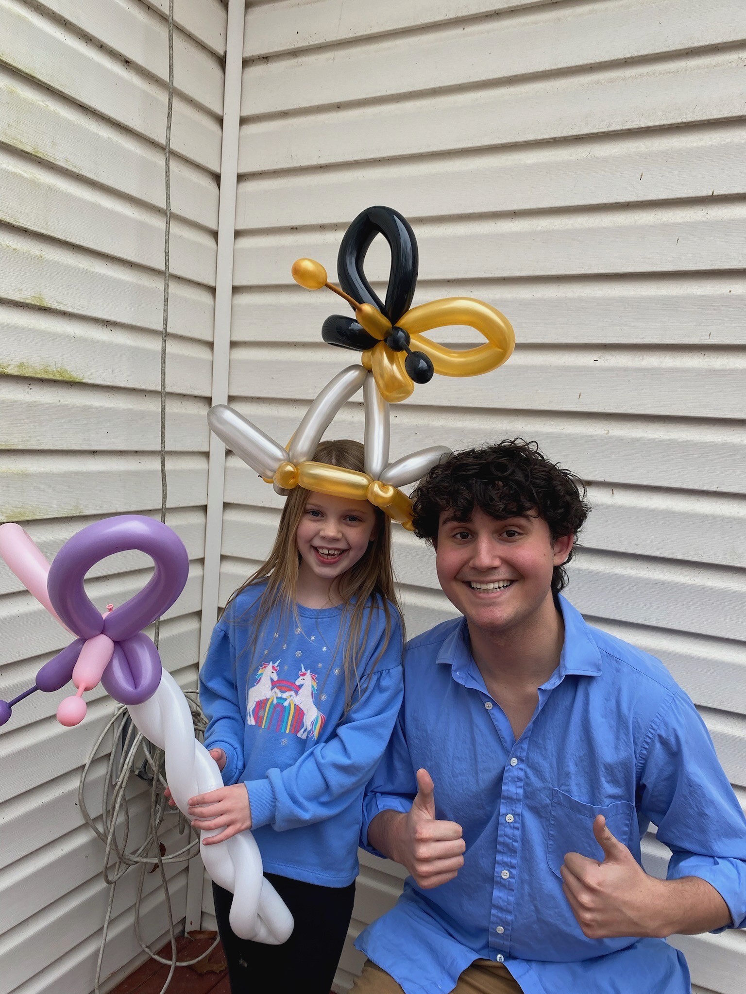 Picture of Daniel wearing a solid blue collared shirt posing with a young girl with a gold and black butterfly birthday hat and purple and pink butterfly wand