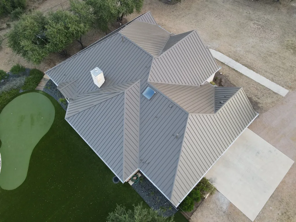 Gray standing seam metal roof with a chimney, skylight and intersecting roof sections in San Antonio, completed in 2023.