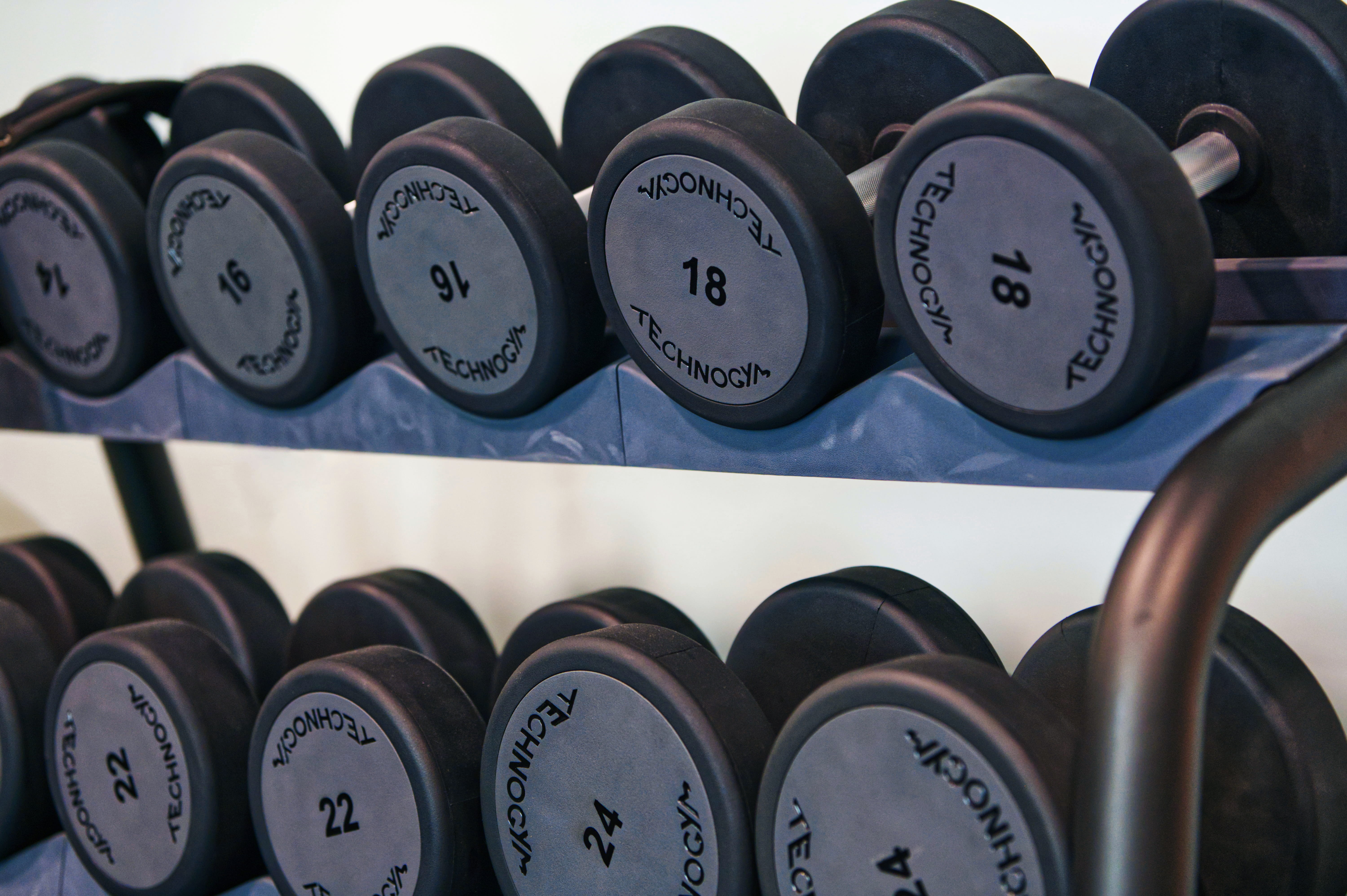 Two men sit at a wooden table with laptops, under a large red lamp. A woman walks by a window. The scene is calm, set against a red-brown wall.