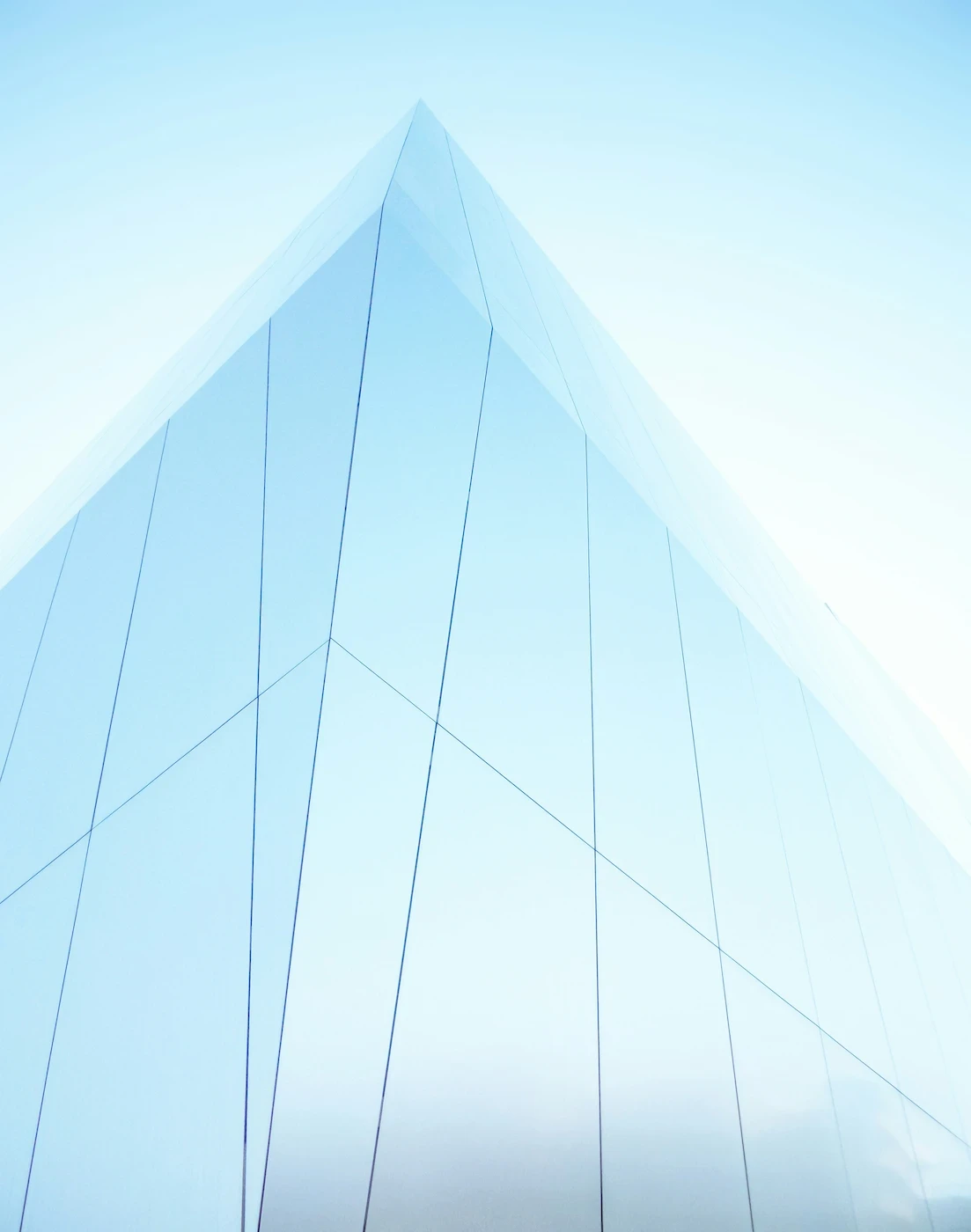 An ultra-minimalist, high-key architectural shot looking up at a bright white and pale blue glass structure. Seamless, clean lines sweep upward, creating a sense of bright, open scale.