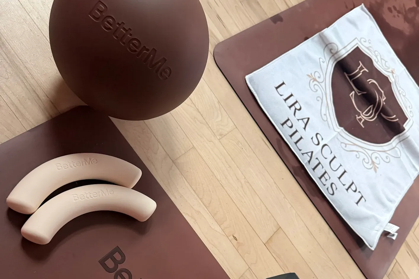 Pilates ball, light weights and block beside a LIRA towel on a mat