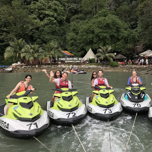 五個人在熱帶環境中乘坐滑水摩托，背景有濃密的樹木和一個標誌，上面寫著「大洋馮大理石地質公園」。