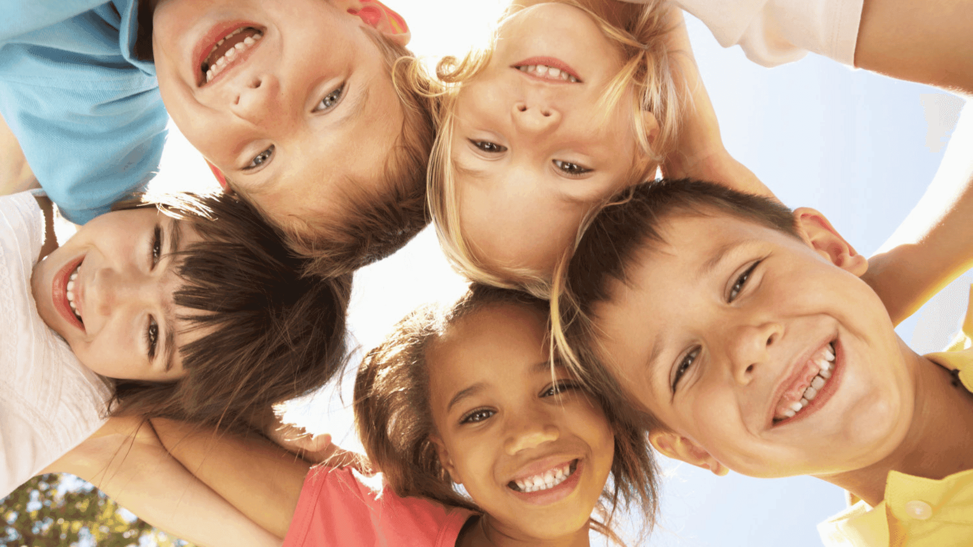 A group of children in a huddle, smiling down at the camera positioned below them in the centre.
