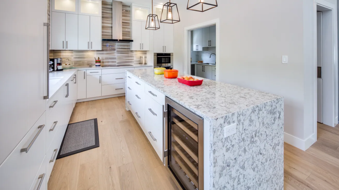Custom luxury kitchen featuring white shaker cabinets, waterfall-edge marble island, stainless steel appliances, and designer pendant lighting