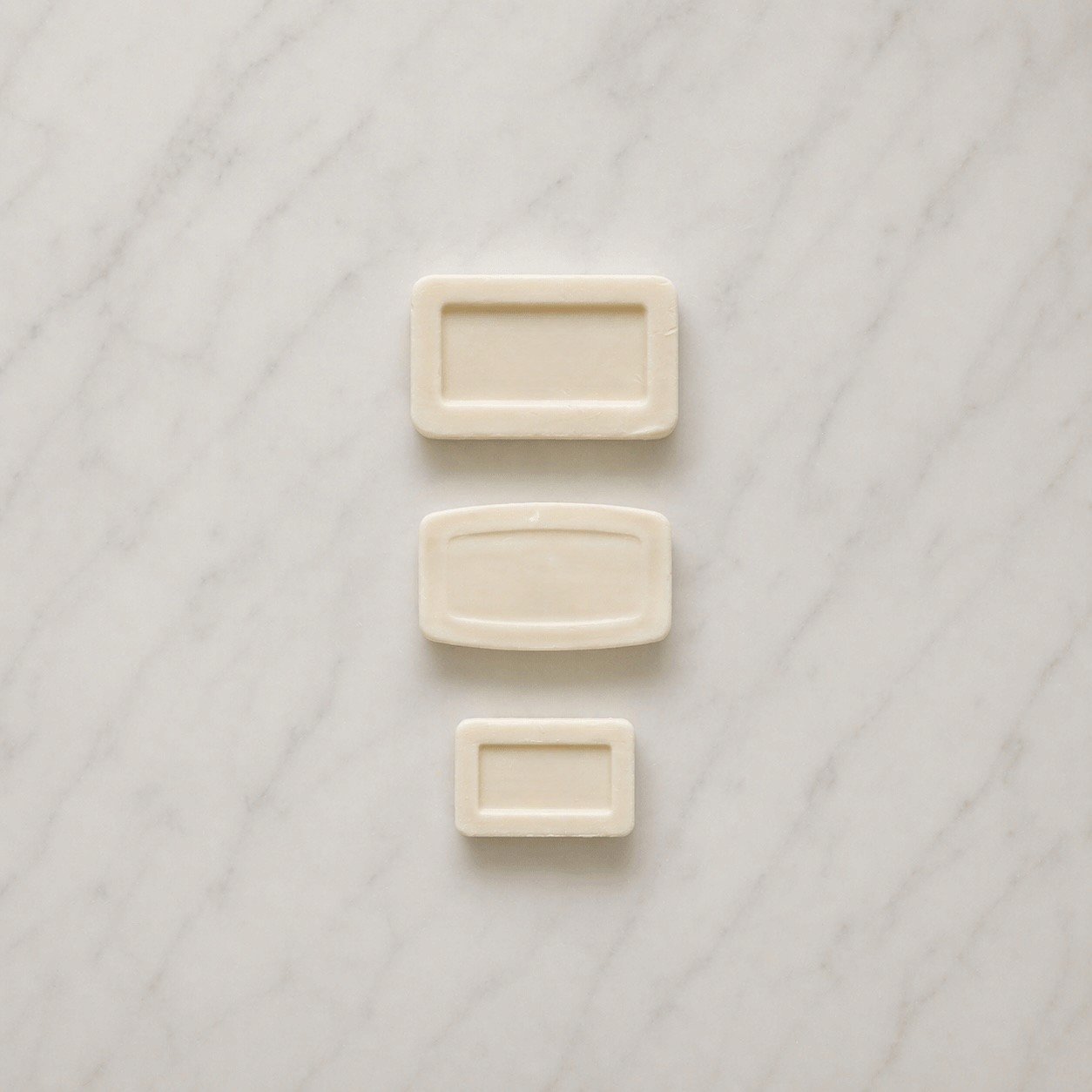 Three Beach Mist bar soaps in different sizes arranged vertically on a light marble hotel bathroom countertop, clean top-down composition with soft natural lighting and ample negative space.