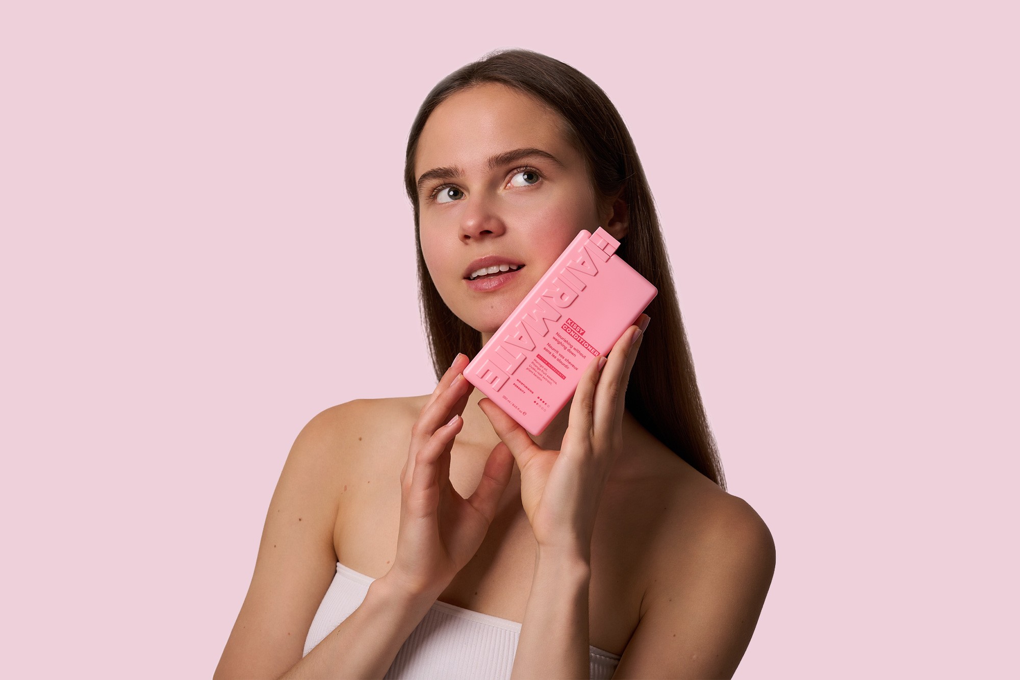 Skaistumkopšanas produktu fotogrāfija ar modeli un rozā HAIRMATE šampūnu uz rozā fona — profesionāla produktu fotosesija Rīgā.