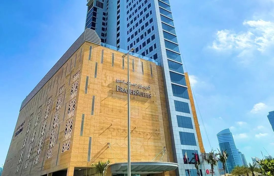 Low-angle view of a luxury high-rise property entrance with modern glass architecture and palm trees.
