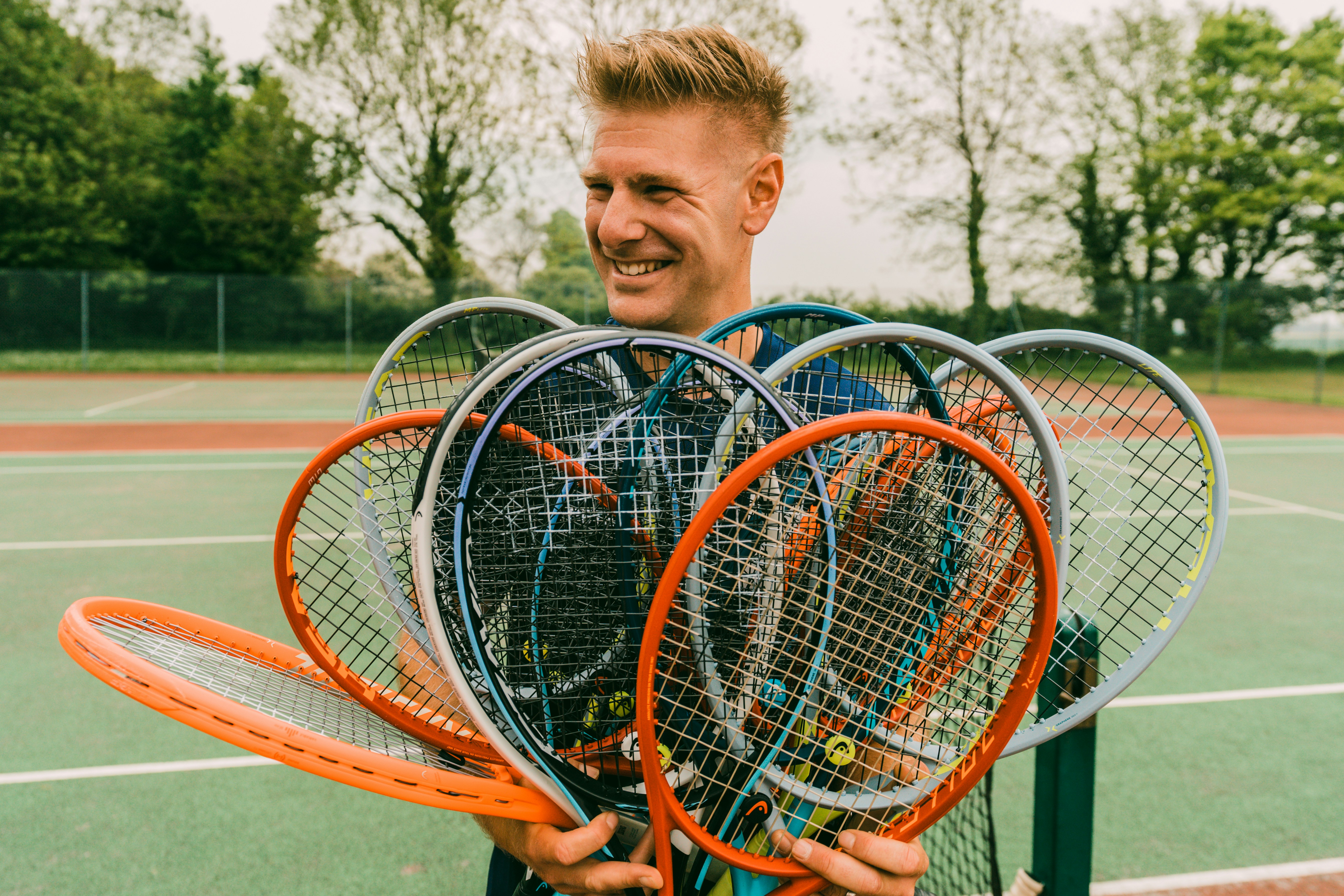 A man holding multiple tennis rackets in a tennis court