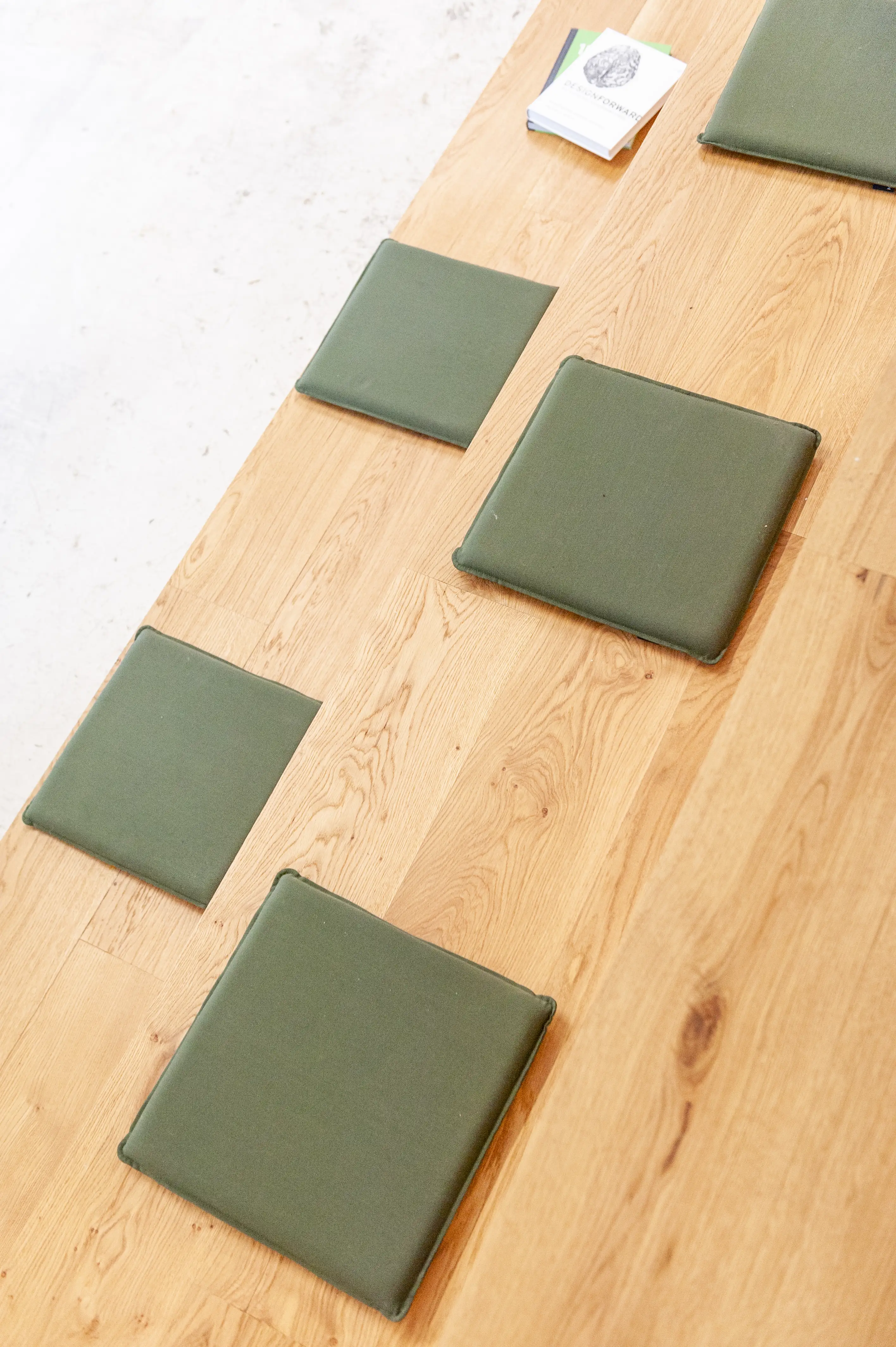 Detail of the oak seating tribune at LA RED with square olive-green cushions arranged on the wooden steps and a small stack of booklets at the top.