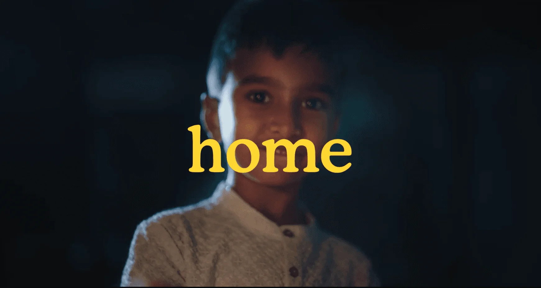 Smiling boy in low light with the word 'home' in yellow, from Dennis Family Homes' film 'For whatever home means to you'
