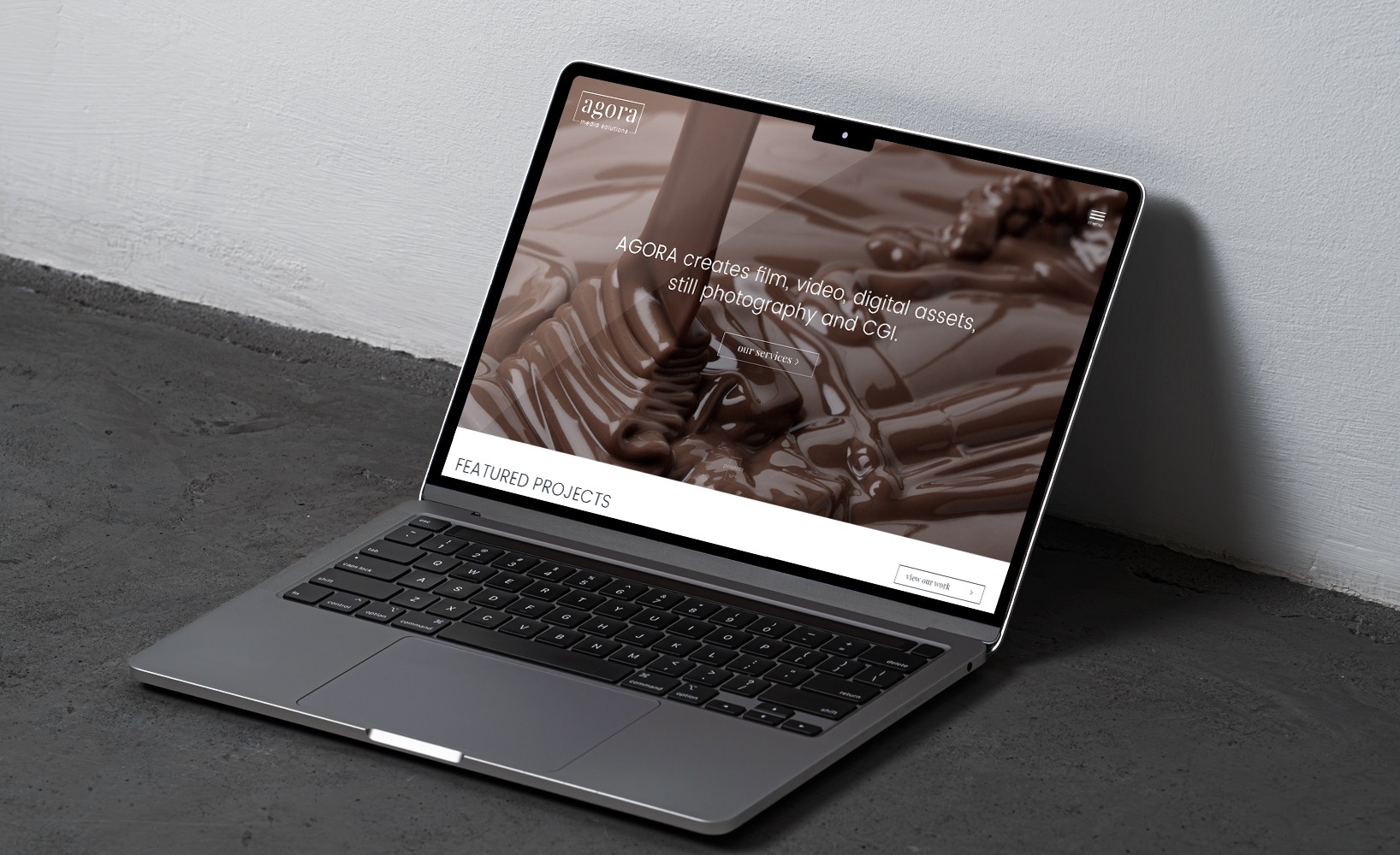 Laptop displaying the Agora Media Solutions website homepage featuring rich melted chocolate background and company tagline.