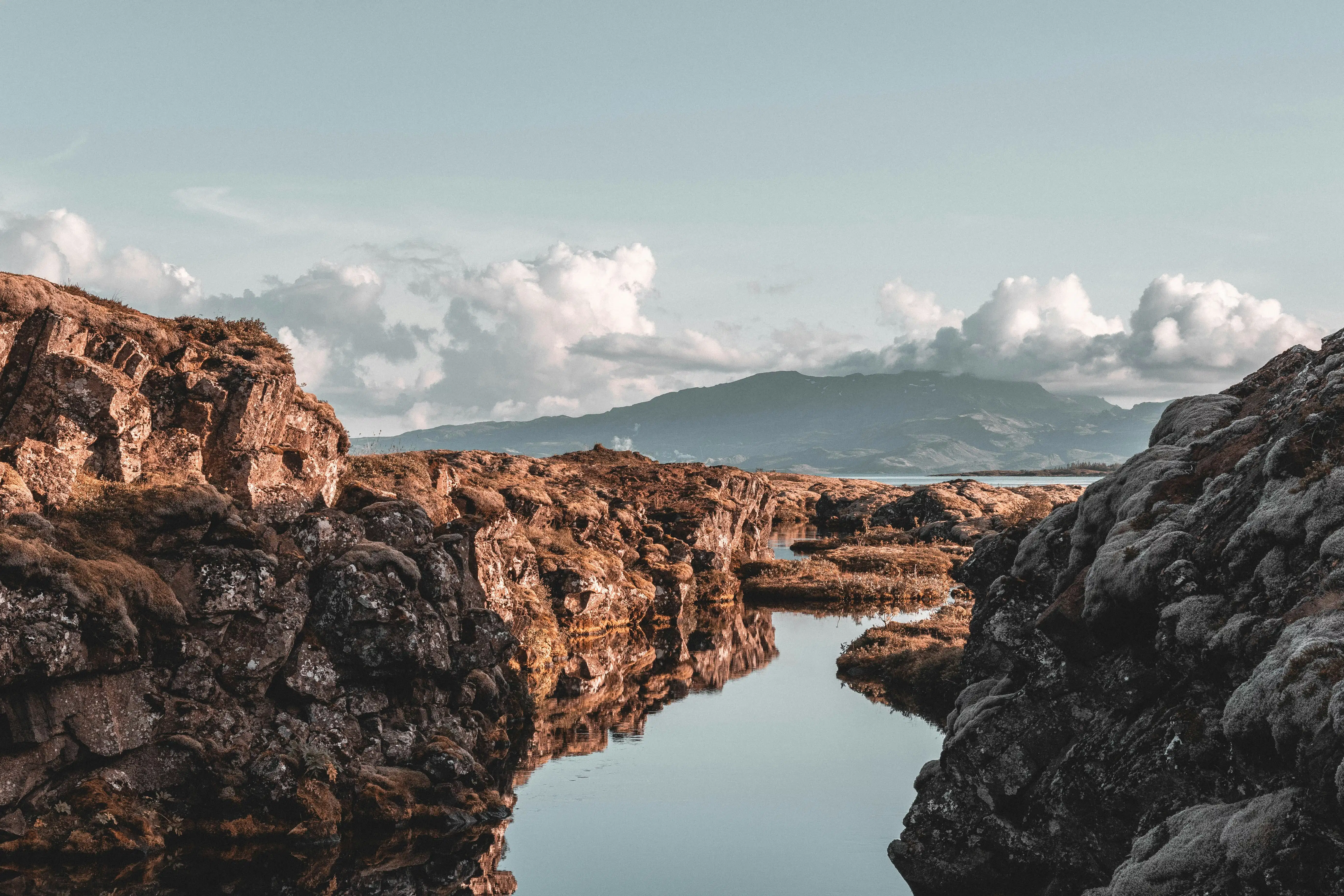 Clear blue water flowing through a rocky rift valley surrounded by rugged cliffs under a cloudy sky.