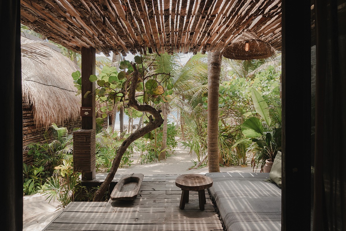 Habitación Estándar en Nômade Tulum, con cama, almohadas y vista a la selva a través de grandes ventanas.