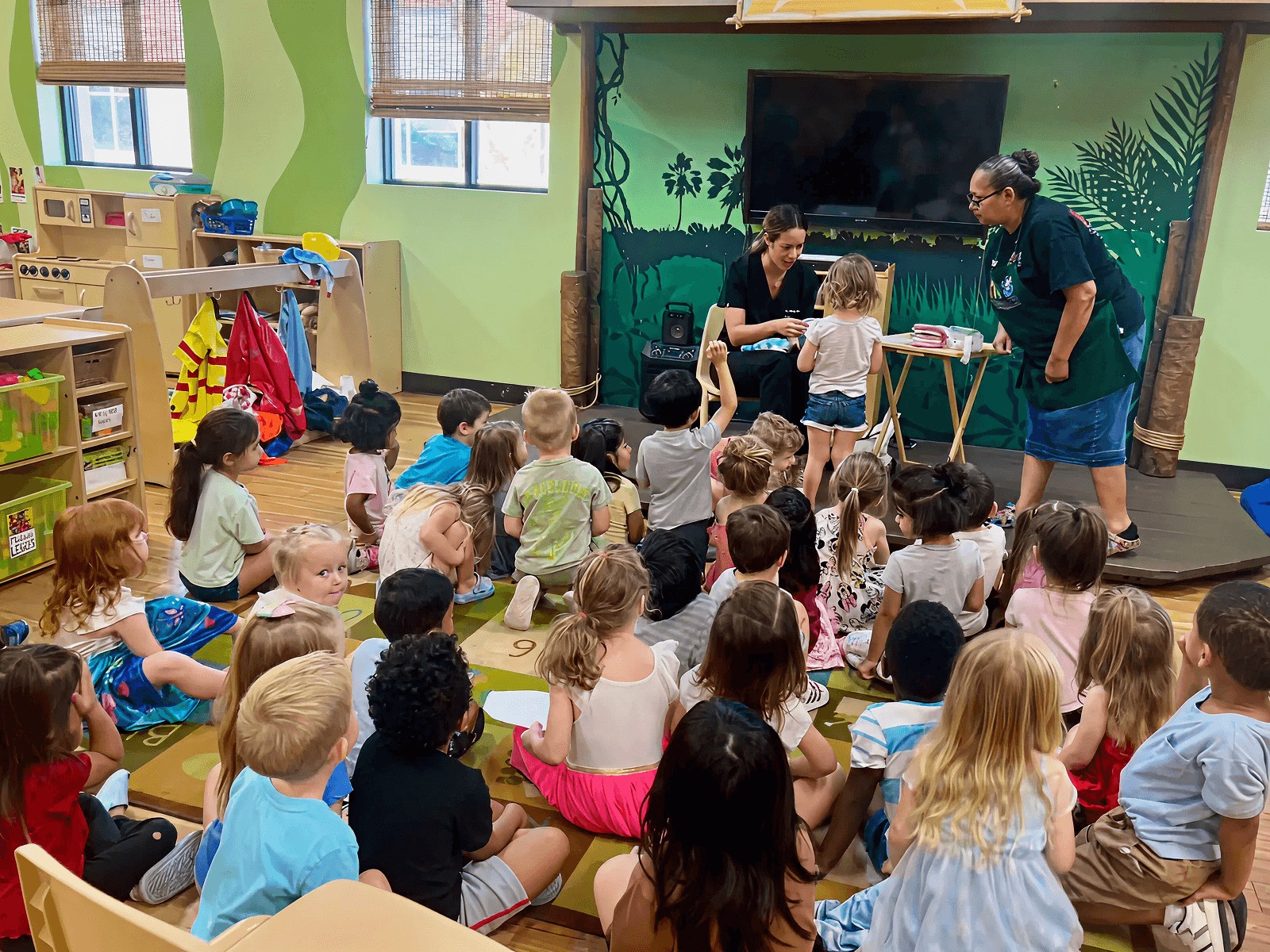 A group of children seated indoors listening to an activity during a community event