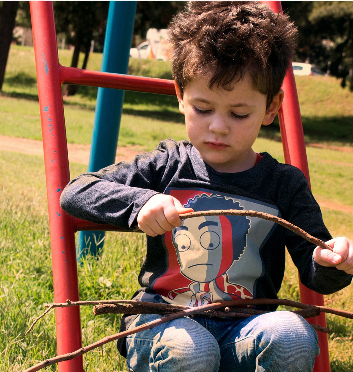 Boy in a playground holding sticks and wearing KN Studios merchandise.