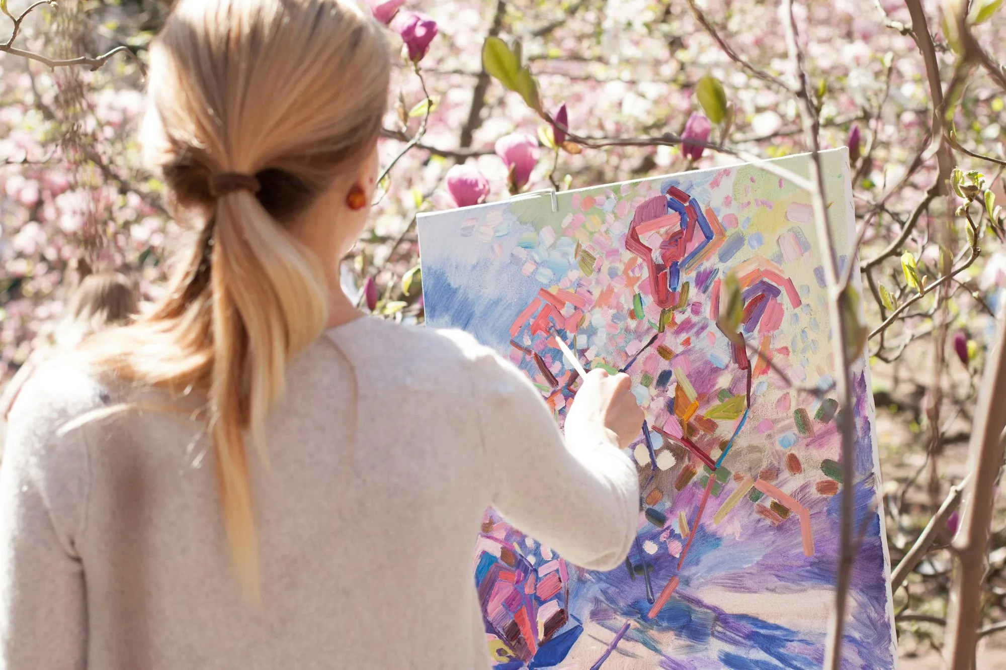 Artist painting a colourful canvas outdoors among flowering trees