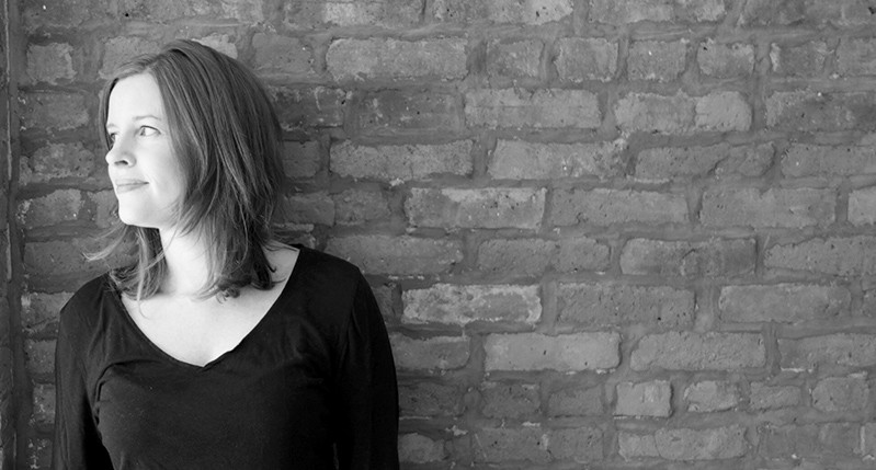 A black and white photo of a woman in front of a brick wall.