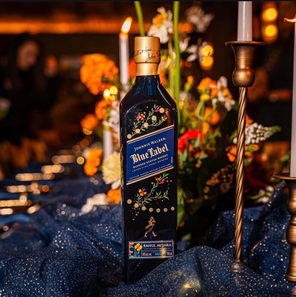 A bottle of Johnnie Walker Blue Label whisky surrounded by a festive arrangement of flowers and candles, set against a sparkling blue cloth.