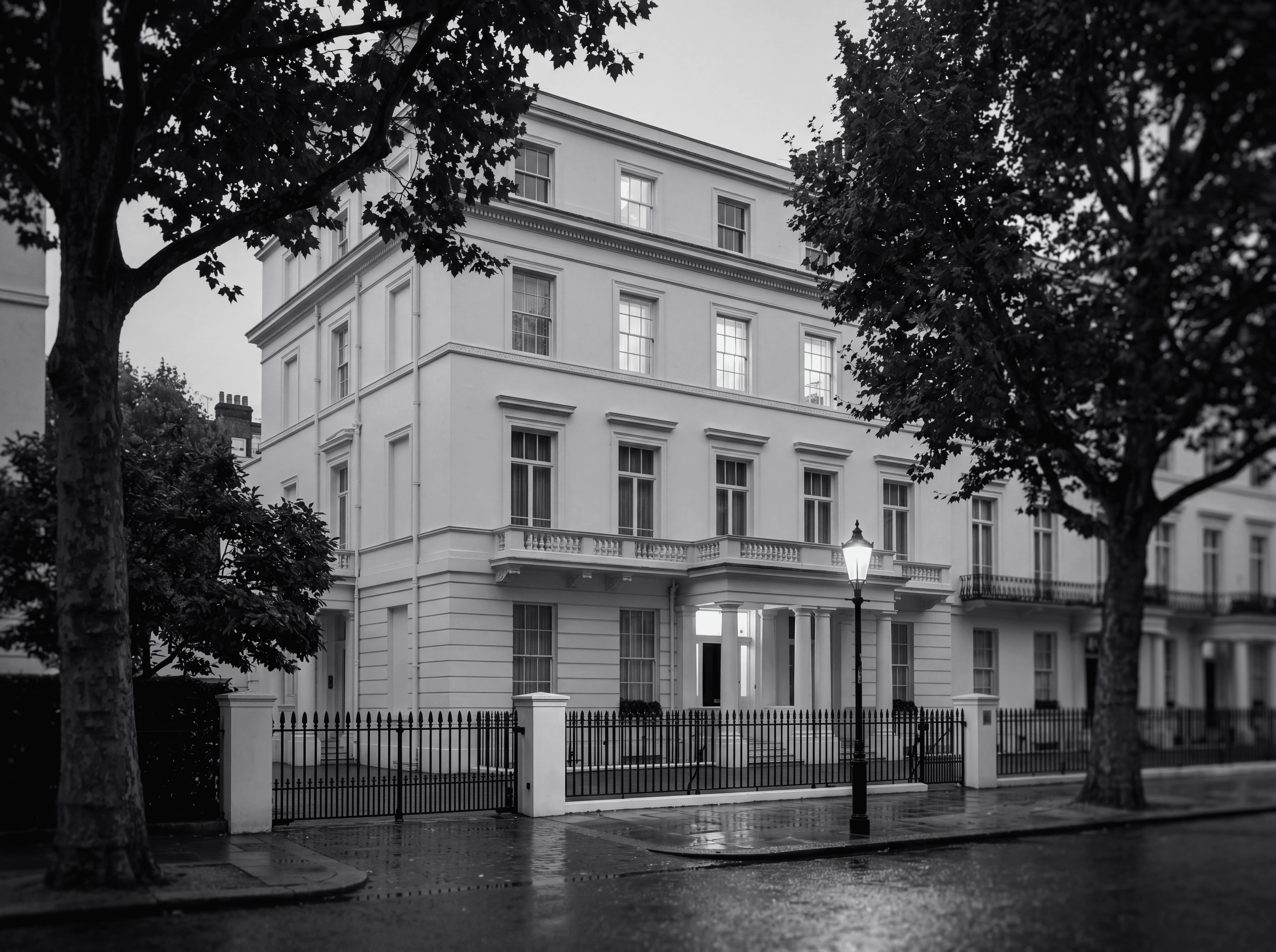 Grand white stucco mansion in Belgravia at dusk with iron railings, illustrating ownership structuring of London property for Russian-speaking families, monochrome editorial photograph