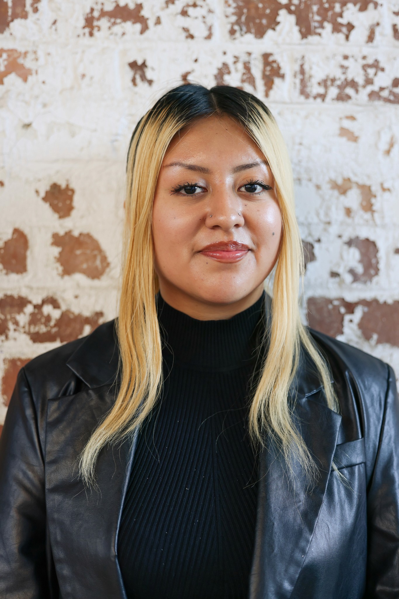 College student smiling at the camera, standing in front of a brick wall. 
