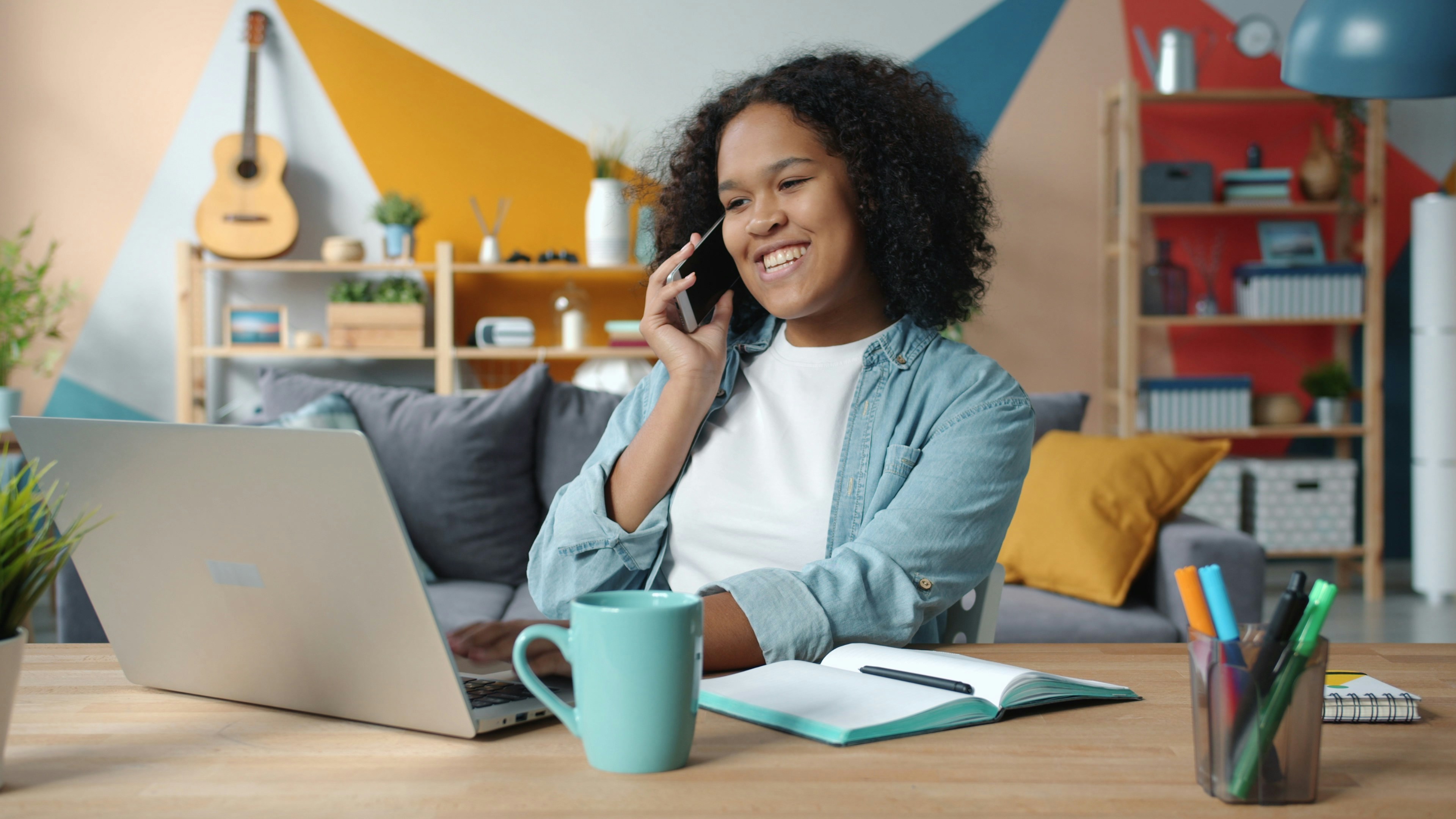 Woman talking on phone while working on laptop at desk.