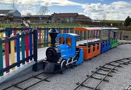Colorful children's miniature train ride with bright blue engine and rainbow carriages in outdoor family attraction