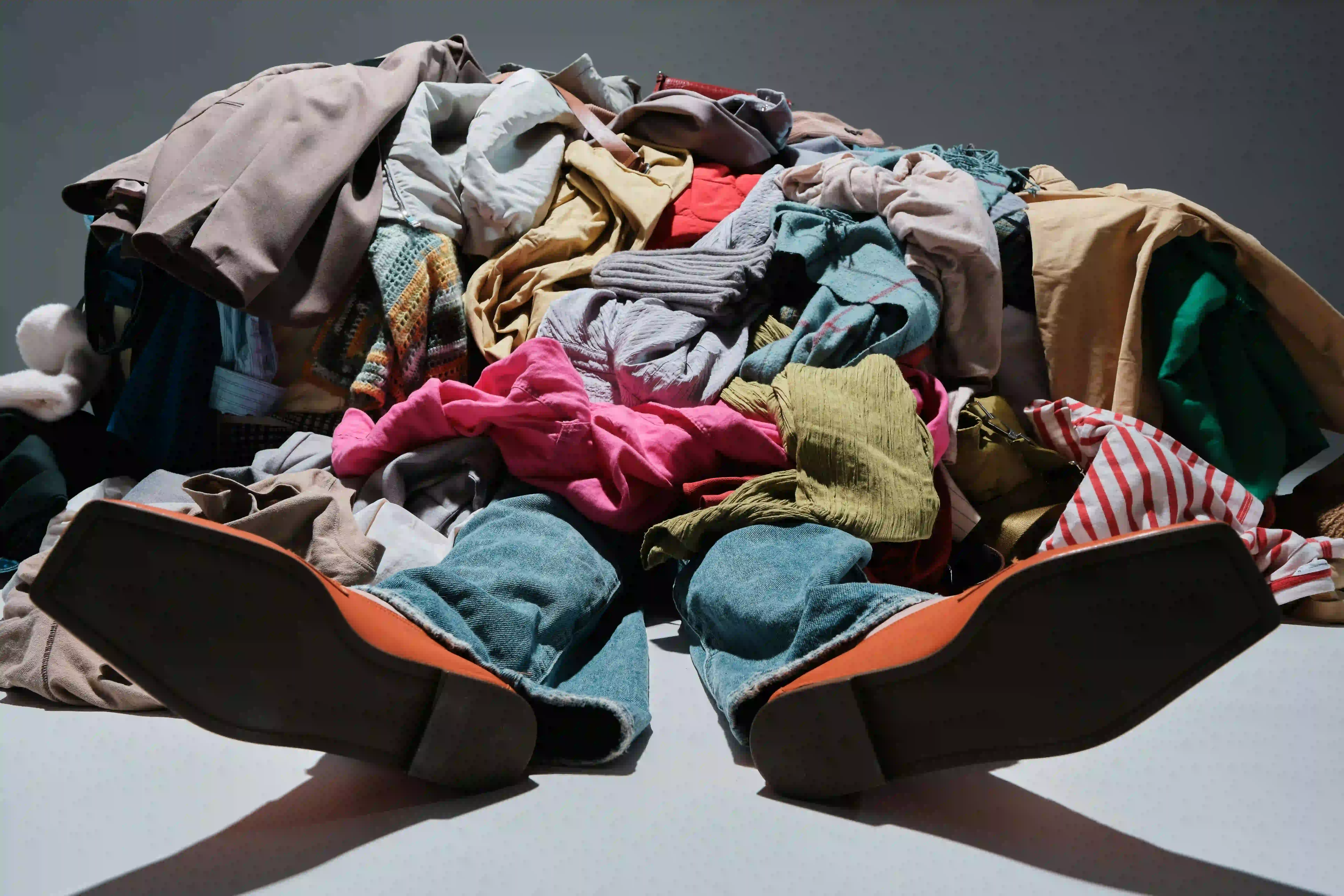 person buried under a pile of brightly coloured clothes to represent the high return rates ecommerce brands face